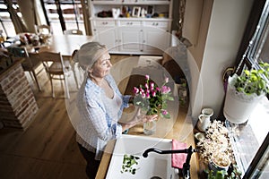 Beautiful mature woman arranging bouquet of roses in a vase, a hobby and relaxation. Older woman living alone, enjoying