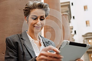 Beautiful mature woman art gallery manager working on tablet while standing in museum hall