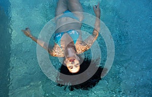 Beautiful mature woman in the best age with dark curly hair in blue bikini in the sun Sunlight floating weightlessly