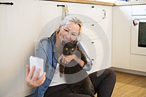 Beautiful mature woman at home, taking selfie with her cat. Older woman living alone, enjoying peaceful weekend day