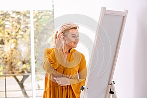 Beautiful mature woman looking at herself in large mirror
