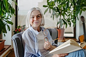 Beautiful mature woman reading book, feeling cozy and happy. Weekend activity for older woman, relaxing at home.