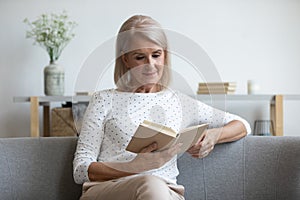 Beautiful mature woman reading book, sitting on couch at home