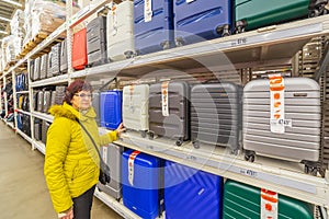 a beautiful mature woman thinking about buying a suitcase on wheels for travel