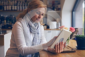 Beautiful mature woman using tablet, sitting in cafe