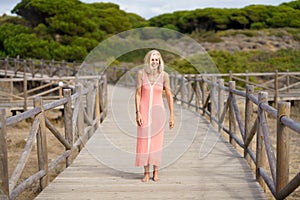 Beautiful mature woman walking along a wooden path near the beach., wearing a nice orange dress.