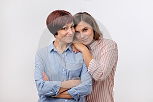 Beautiful maturesenior mom and her adult daughter are hugging, looking at camera and smiling.