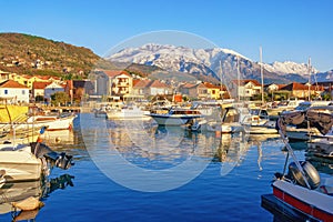 Beautiful Mediterranean landscape on sunny winter day. Fishing boats in harbor and snow-capped mountains. Montenegro, Tivat city