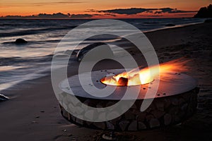 The beautiful metal round a fireplace stands on the sandy coast with a tidal wave at sunset, stones, sand, waves, the