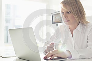 Beautiful mid adult businesswoman using laptop while having coffee at home