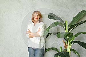 Beautiful mid adult woman smiling on grey background with green plant