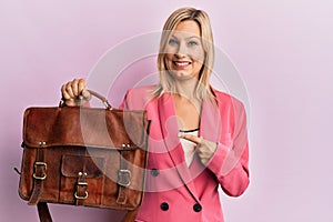Beautiful middle age blonde woman holding business bag smiling happy pointing with hand and finger