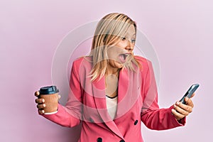 Beautiful middle age blonde woman using smartphone and drinking a cup of coffee celebrating crazy and amazed for success with open