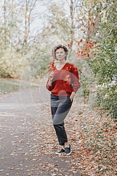 Beautiful middle age Caucasian woman with short curly hair in park outdoor. Young woman with in casual clothes holding autumn fall