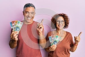 Beautiful middle age couple holding australian dollars smiling happy pointing with hand and finger to the side