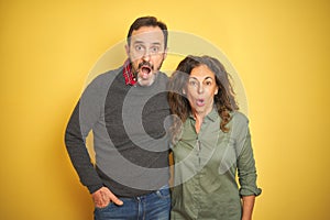 Beautiful middle age couple over isolated yellow background afraid and shocked with surprise expression, fear and excited face