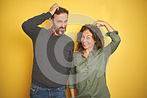 Beautiful middle age couple over isolated yellow background confuse and wonder about question