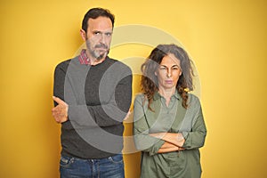 Beautiful middle age couple over isolated yellow background skeptic and nervous, disapproving expression on face with crossed arms