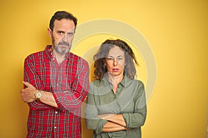 Beautiful middle age couple over isolated yellow background skeptic and nervous, disapproving expression on face with crossed arms