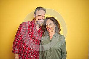 Beautiful middle age couple over isolated yellow background winking looking at the camera with sexy expression, cheerful and happy