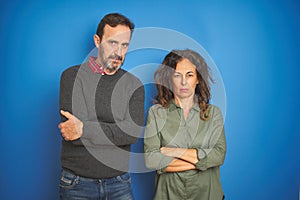 Beautiful middle age couple together standing over isolated blue background skeptic and nervous, disapproving expression on face