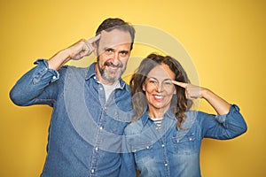 Beautiful middle age couple together standing over isolated yellow background Smiling pointing to head with one finger, great idea