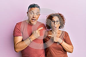 Beautiful middle age couple together wearing casual clothes surprised pointing with finger to the side, open mouth amazed