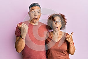 Beautiful middle age couple together wearing casual clothes surprised pointing with hand finger to the side, open mouth amazed