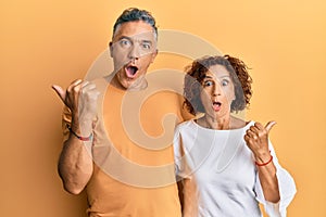 Beautiful middle age couple together wearing casual clothes surprised pointing with hand finger to the side, open mouth amazed