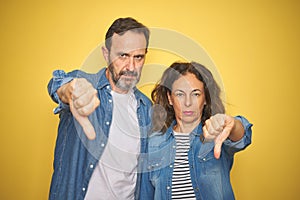 Beautiful middle age couple together wearing denim shirt over isolated yellow background looking unhappy and angry showing