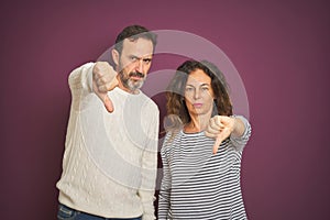 Beautiful middle age couple wearing winter sweater over isolated purple background looking unhappy and angry showing rejection and