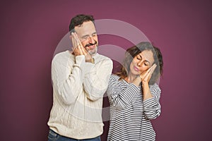 Beautiful middle age couple wearing winter sweater over isolated purple background sleeping tired dreaming and posing with hands