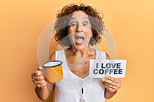 Beautiful middle age mature woman holding i love coffee banner celebrating crazy and amazed for success with open eyes screaming