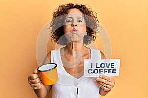 Beautiful middle age mature woman holding i love coffee banner puffing cheeks with funny face