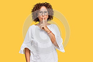 Beautiful middle age mature woman wearing casual clothes and glasses asking to be quiet with finger on lips