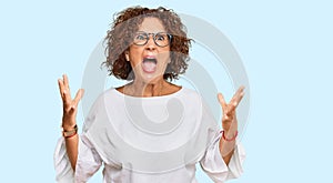 Beautiful middle age mature woman wearing casual clothes and glasses crazy and mad shouting and yelling with aggressive expression