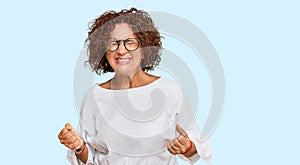 Beautiful middle age mature woman wearing casual clothes and glasses very happy and excited doing winner gesture with arms raised,