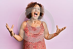 Beautiful middle age mature woman wearing summer dress crazy and mad shouting and yelling with aggressive expression and arms