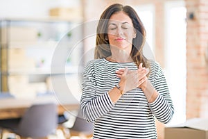 Beautiful middle age senior woman standing smiling with hands on chest with closed eyes and grateful gesture on face