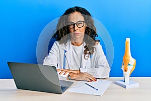 Beautiful middle age woman doctor at orthopedic clinic skeptic and nervous, frowning upset because of problem