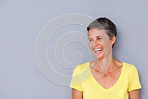 Beautiful middle age woman laughing by gray wall