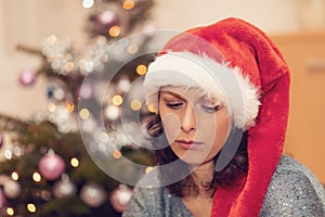 Beautiful middle age woman in santa hat sitting near the Christmas tree