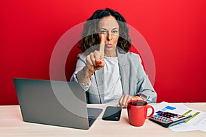 Beautiful middle age woman working at the office drinking a cup of coffee pointing with finger up and angry expression, showing no