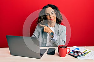 Beautiful middle age woman working at the office drinking a cup of coffee pointing with hand finger to the side showing