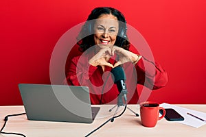 Beautiful middle age woman working at radio studio smiling in love doing heart symbol shape with hands