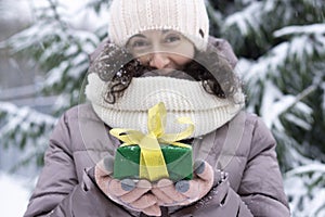 A beautiful middle-aged 45-year-old woman holding a nice Christmas present in the air. Snowy landscape with spruce and snow