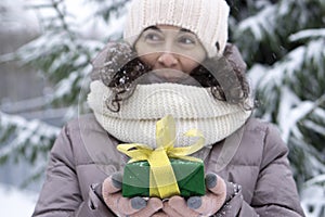 A beautiful middle-aged 45-year-old woman holding a nice Christmas present in the air. Snowy landscape with spruce and snow