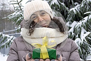 A beautiful middle-aged 45-year-old woman holding a nice Christmas present in the air. Snowy landscape with spruce and snow