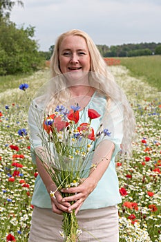 beautiful middle-aged blonde woman stands among a flowering field of poppies