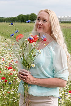 beautiful middle-aged blonde woman stands among a flowering field of poppies